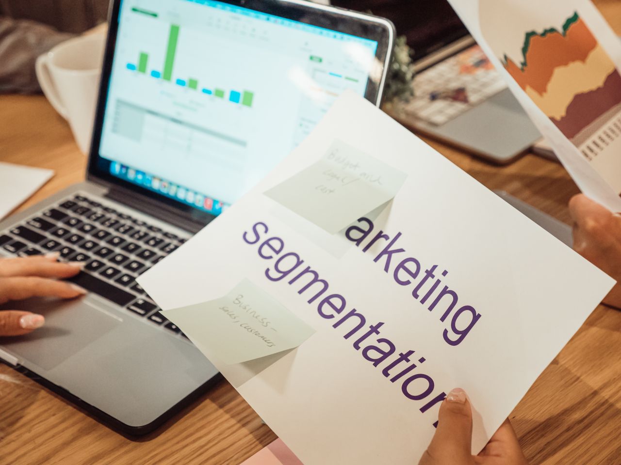Uno spazio di lavoro moderno con mani che analizzano dati di marketing su un laptop e documenti cartacei.